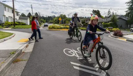 Man and kids biking in foreground and two pedestrians crossing street in background