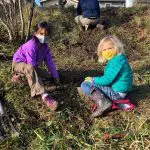 two kids in natural space helping plant a tree