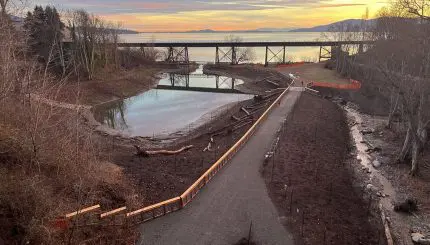 An estuary that connects to the bay is located next to a walking trail with a sunset in the background