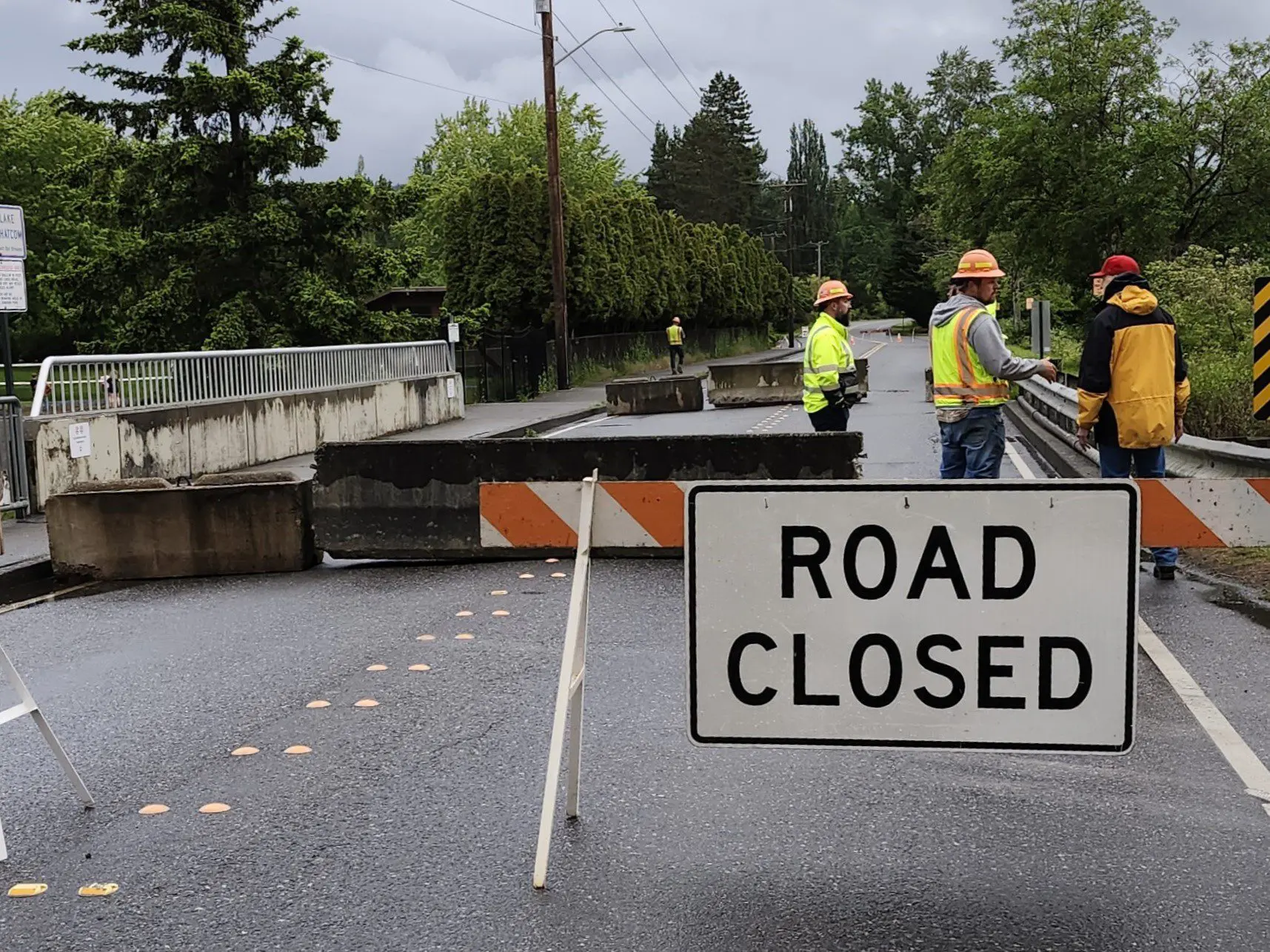 Road closure sign in road with vehicle bridge and construction workers in the background