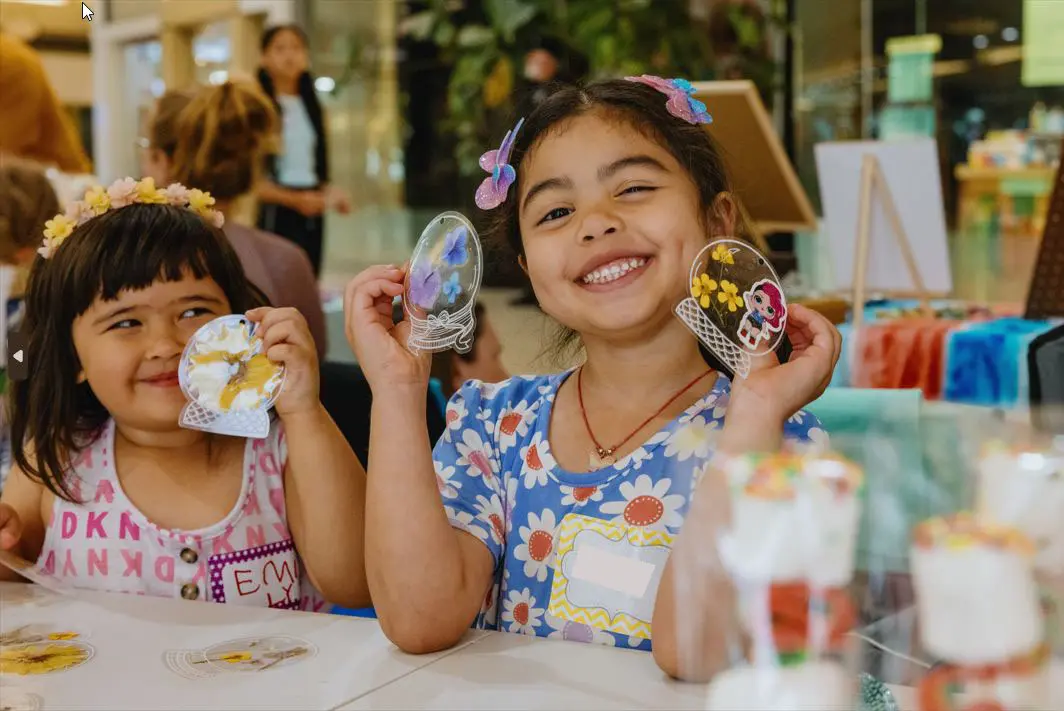 Two young girls smile while holding their craft projects.