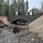 Arch culvert over creek with erosion control mats on steep streambanks and excavator working above the culvert