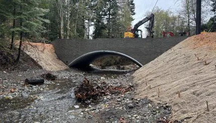Arch culvert over creek with erosion control mats on steep streambanks and excavator working above the culvert