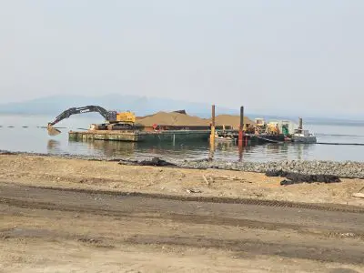 Barge in water off of shoreline with excavator and sand on it