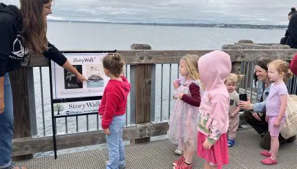 A woman explains a boardwalk sign to a group of young children