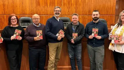 City Councilmembers pose in City Council Chambers, each holding a copy of Red Paint.