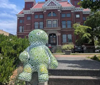 A statue of a small, green and white creature in front of a historic building
