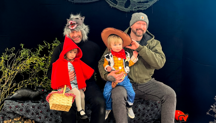 Two men pose with children in Halloween costumes (a Little Red Riding Hood and a Woody from Toy Story)