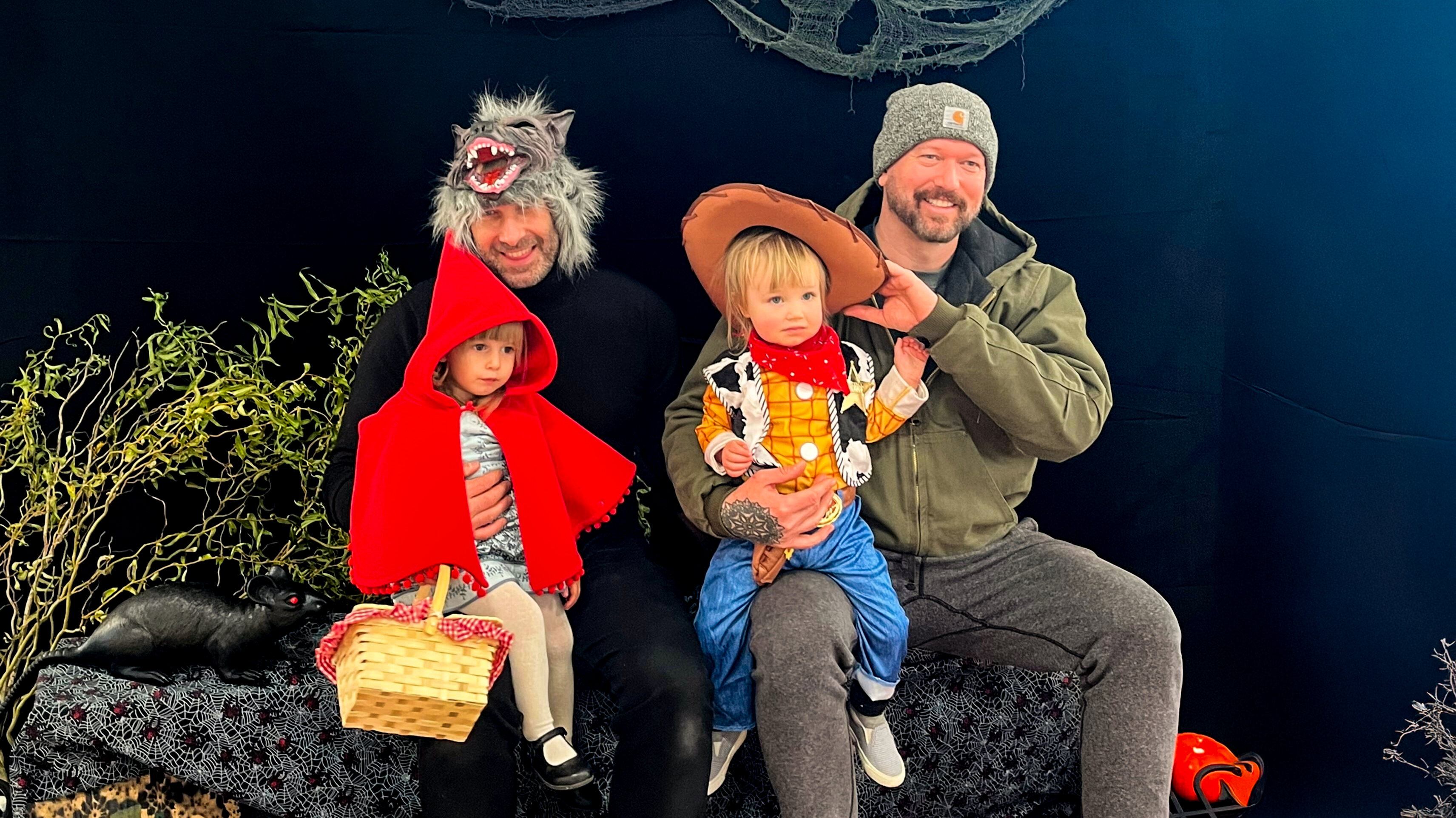 Two men pose with children in Halloween costumes (a Little Red Riding Hood and a Woody from Toy Story)