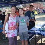 Three people standing at an informational table outside smiling.