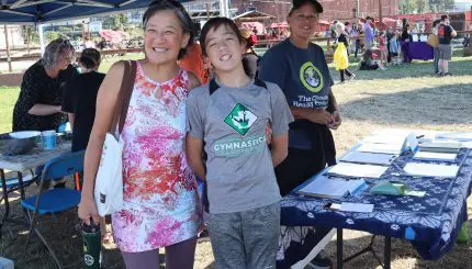 Three people standing at an informational table outside smiling.