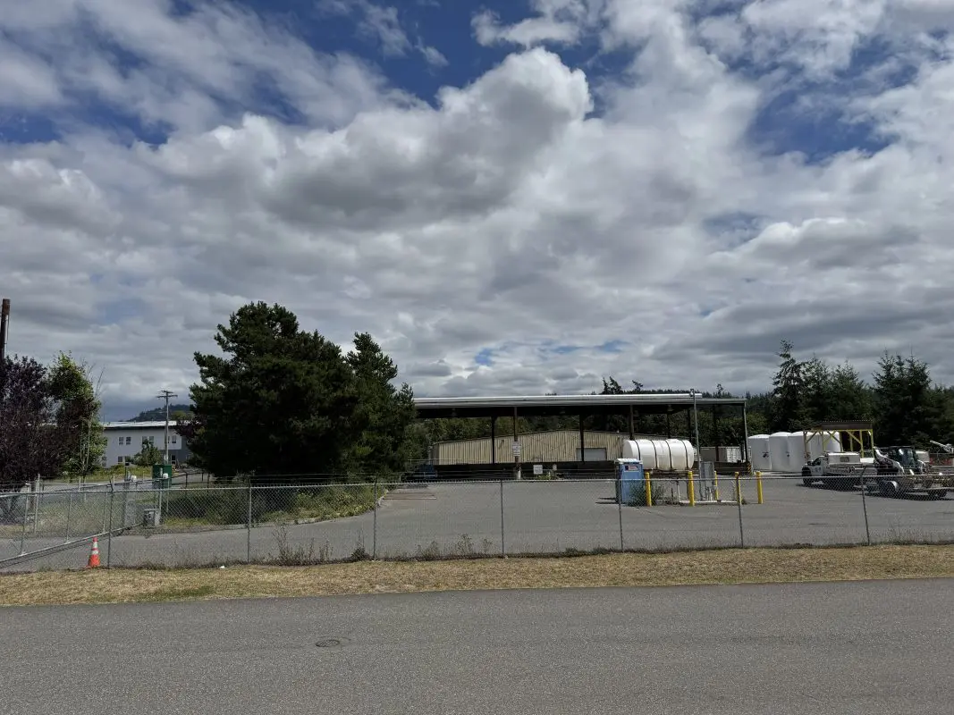 A fenced parking lot with large equipment in the background