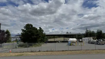 A fenced parking lot with large equipment in the background