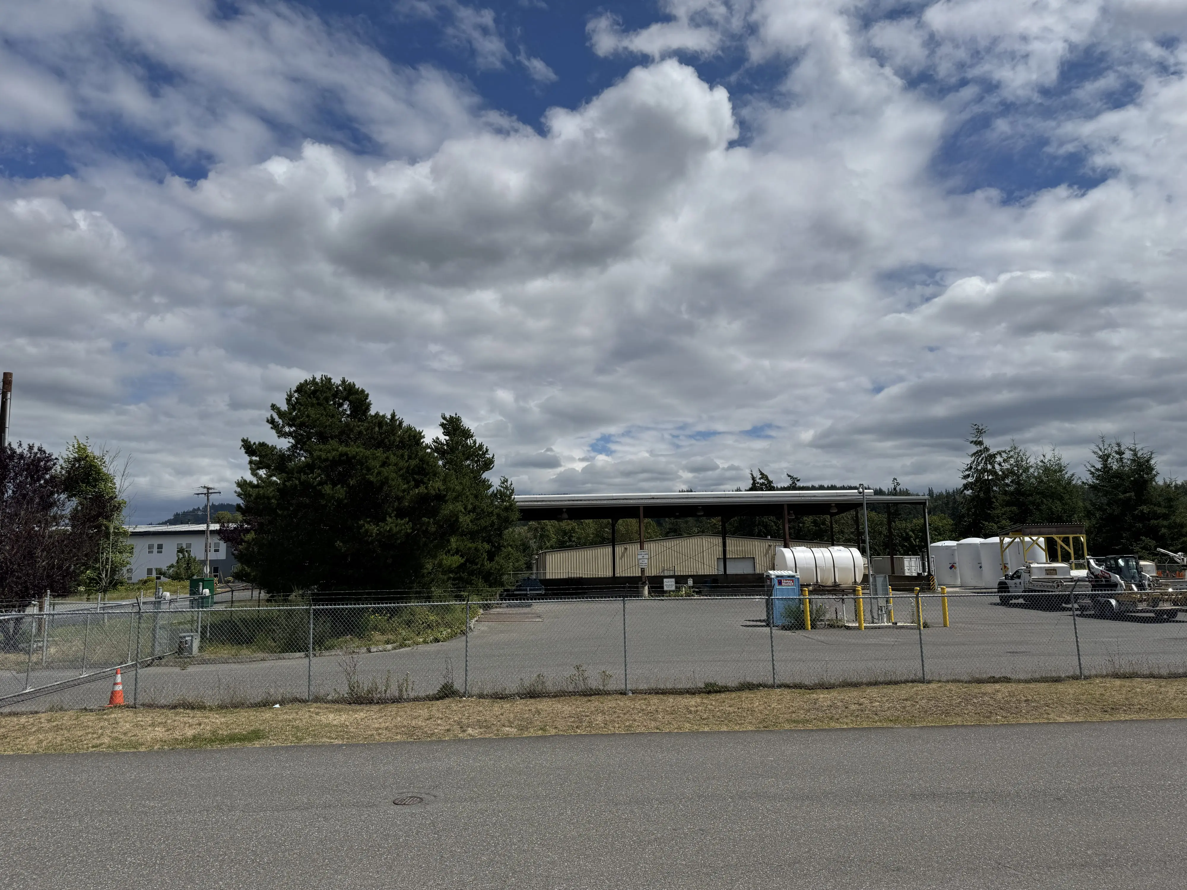 A fenced parking lot with large equipment in the background