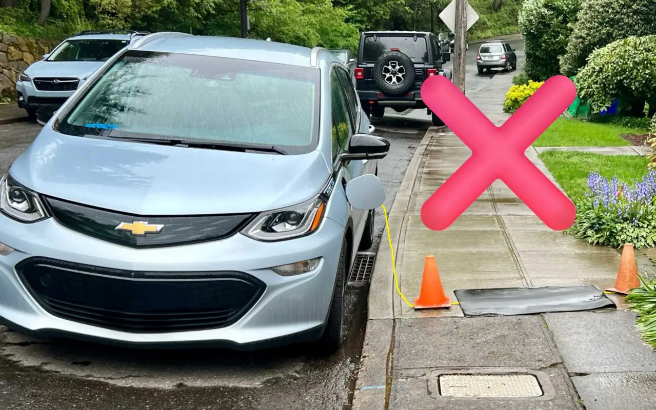 A parked electric vehicle with a charging cord on the sidewalk.