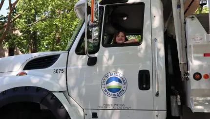 little girl sitting inside the cab of white City of Bellingham dump truck