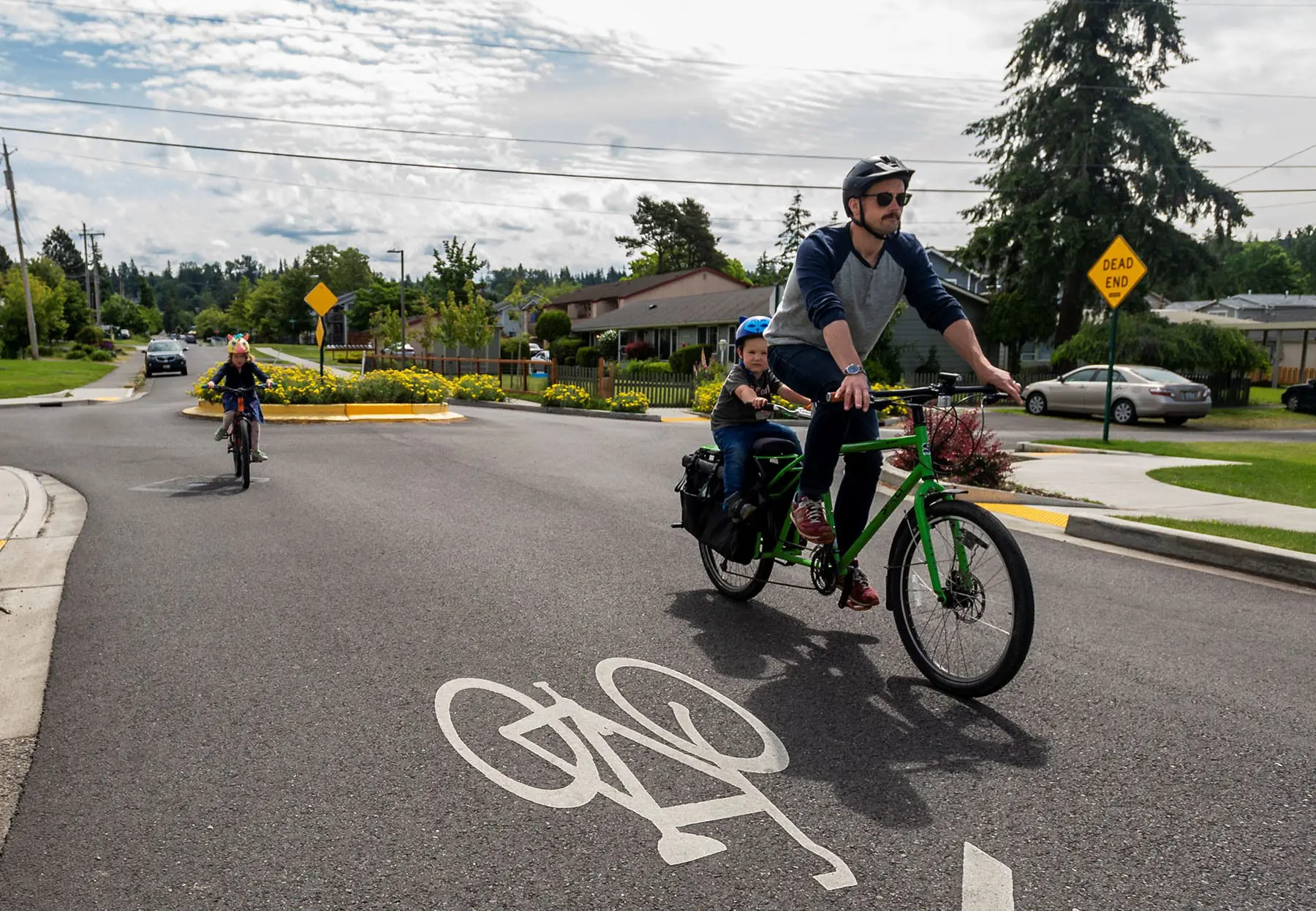 Man and young child riding on bike with older child riding near by