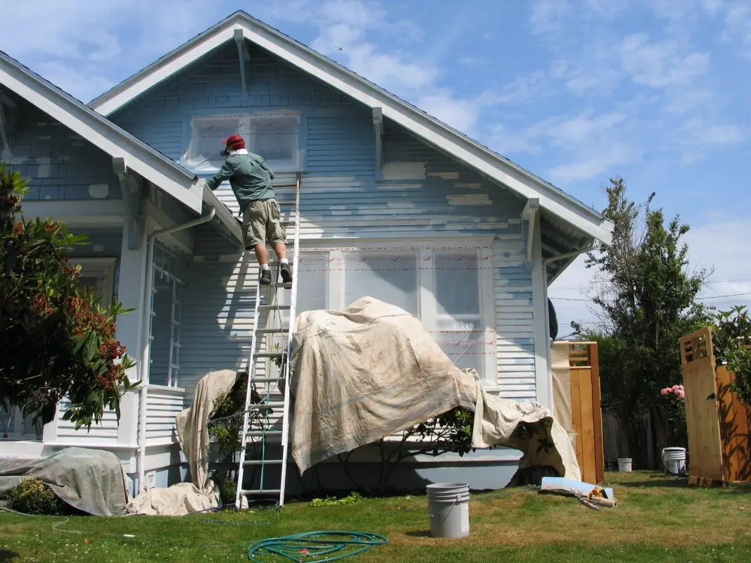 Someone on a ladder painting the side of a house.