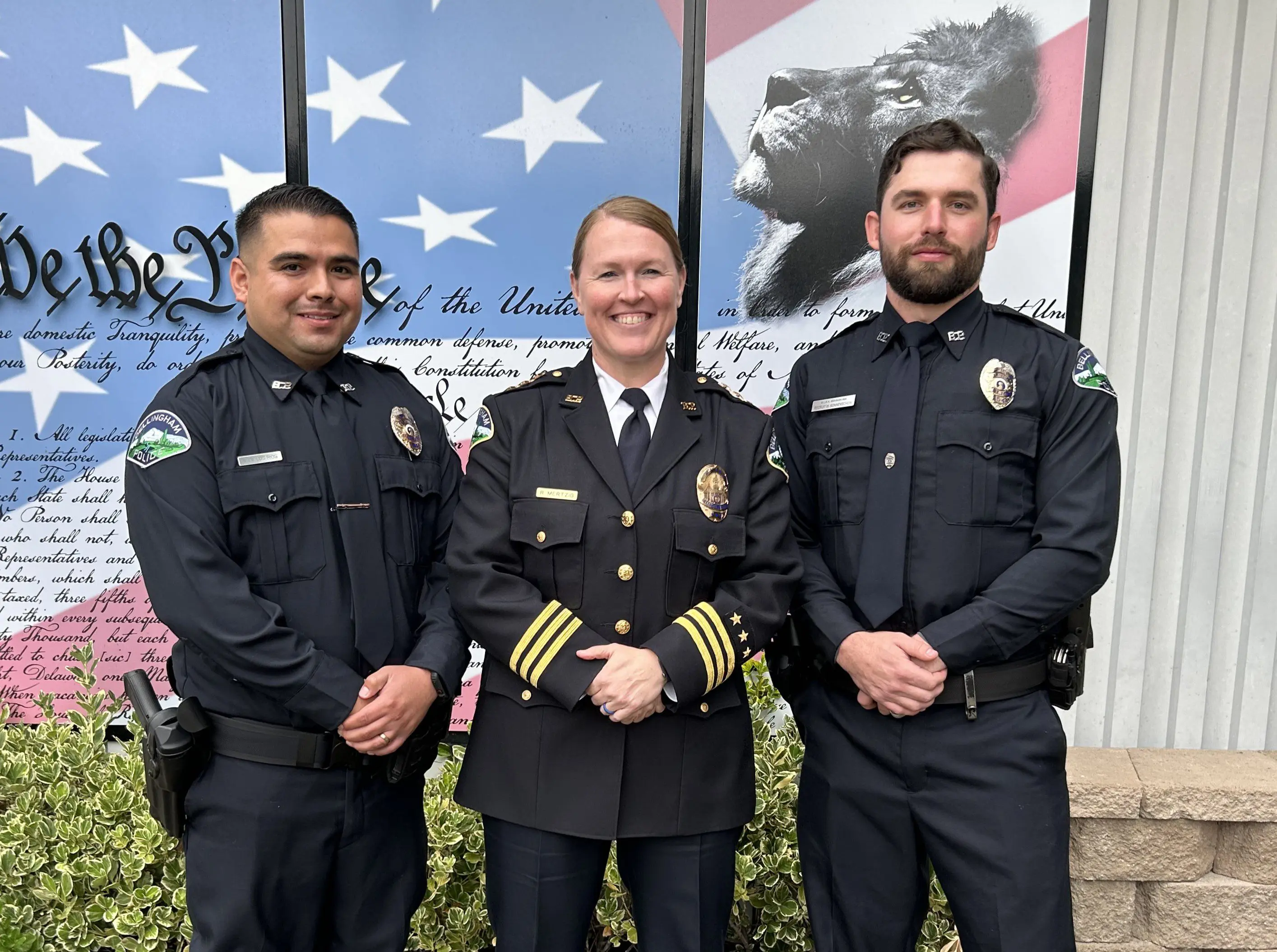 three police officers posing together in full uniforms, smiling