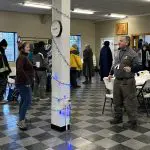 Two shelter workers talk. Shelter guests wait in a line in the background.