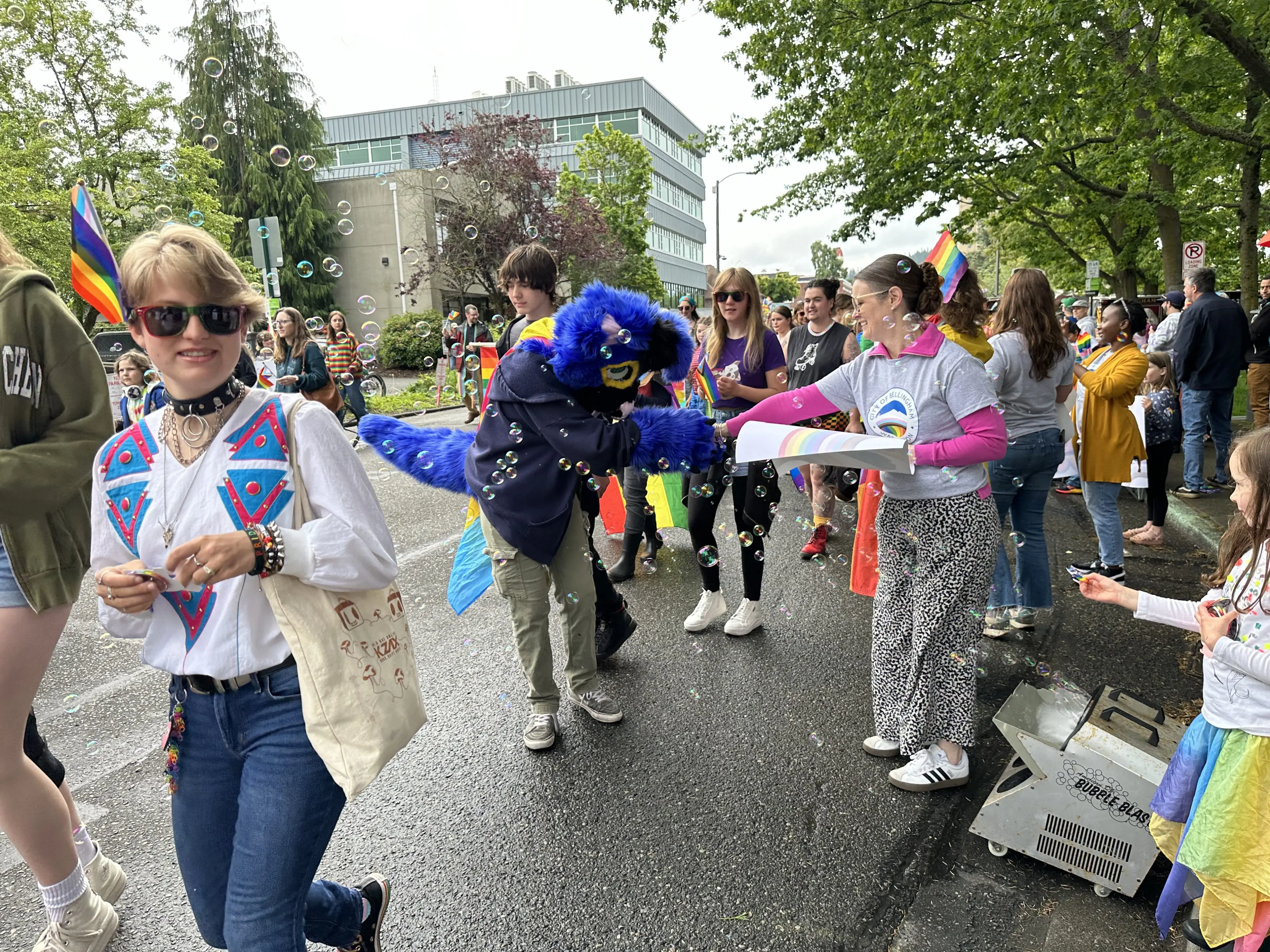 A woman wearing a City of Bellingham t-shirt hands a sticker to someone marching in the Whatcom Youth Pride parade