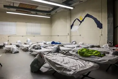 Cots are lined up inside a large room