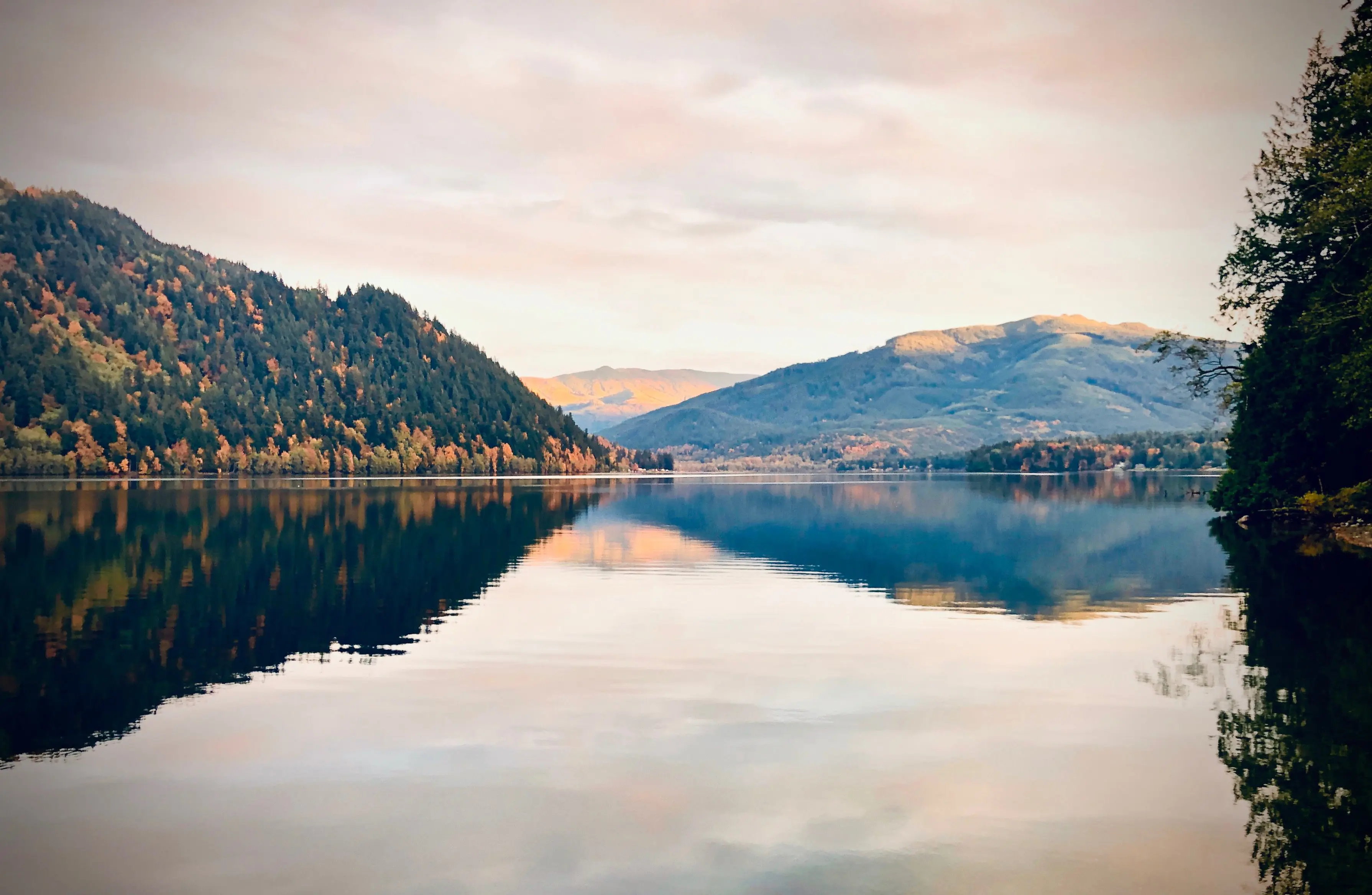 Sunset photo of Lake Whatcom with reflection of trees and hillsides in the lake water.