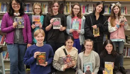 Ten teens standing together in library each holding a book