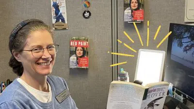A library staff person is using a light therapy lamp. The lamp is highlighted by illustrated yellow lines.