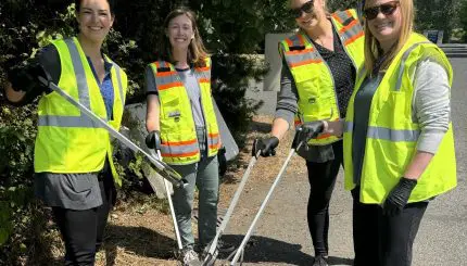 4 people smiling while using litter grabbers to put litter in a bucket