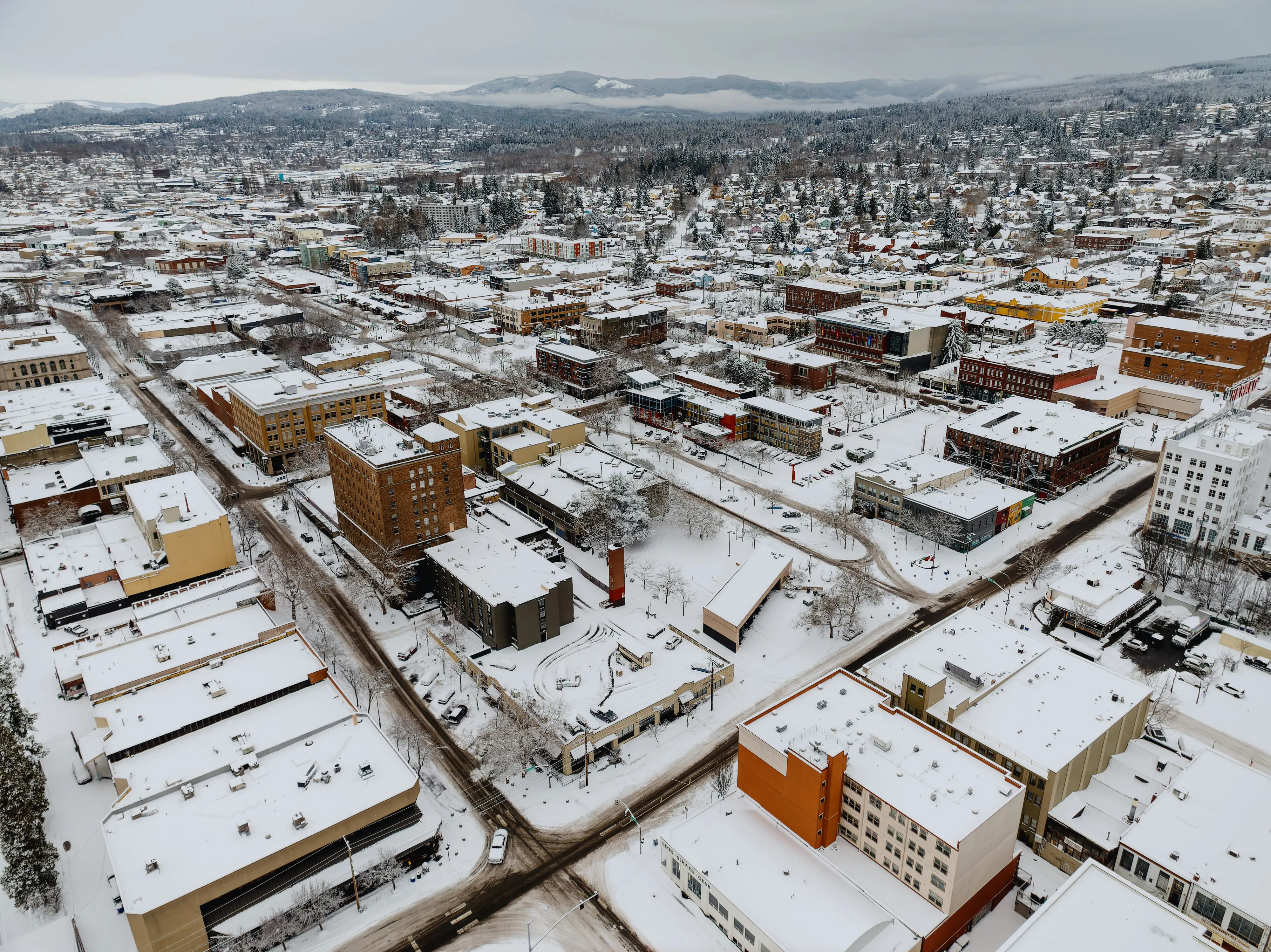 Aerial photo of snow covered downtown Bellingham buildings with snowy, treed hills in distance