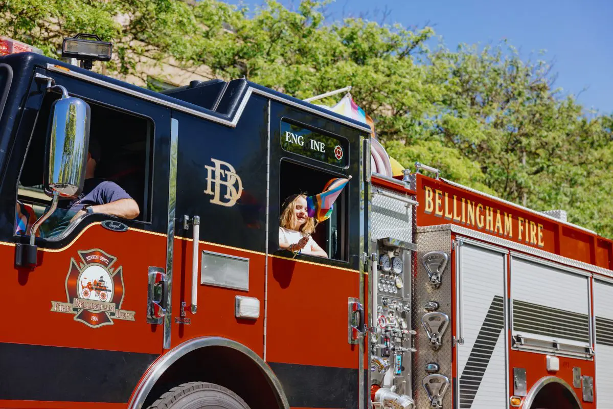 A child waves a rainbow flag from a fire truck