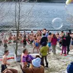 A crowd of a couple hundred people run into a lake in winter