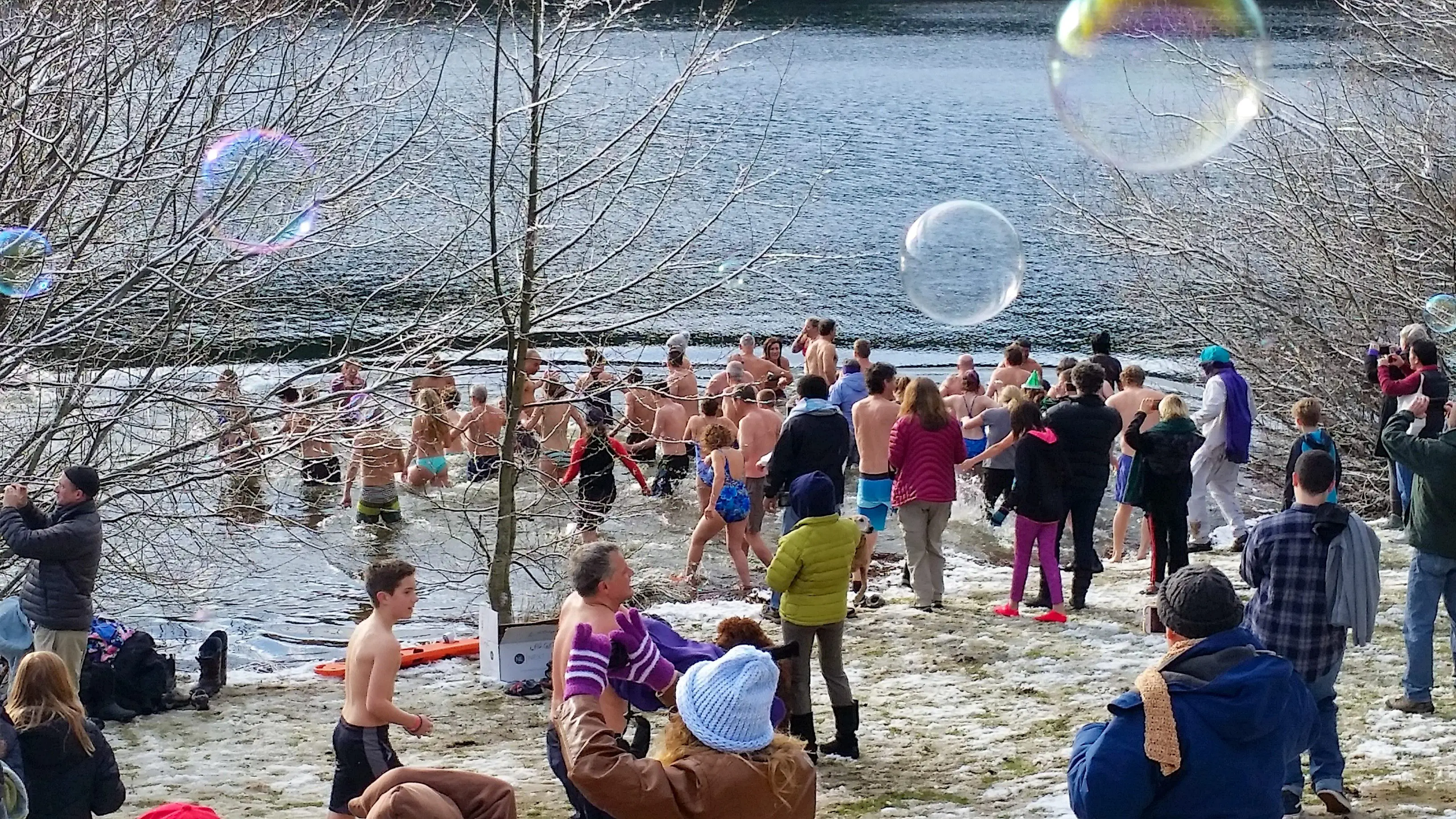 A crowd of a couple hundred people run into a lake in winter