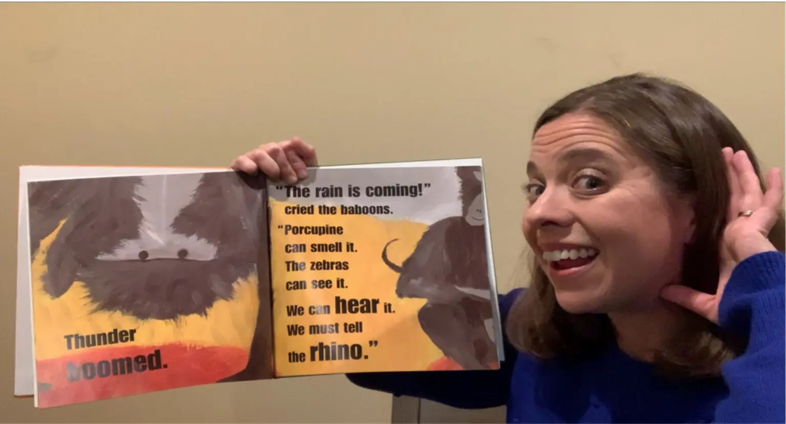 Person smiling and holding up a children's book about animals.