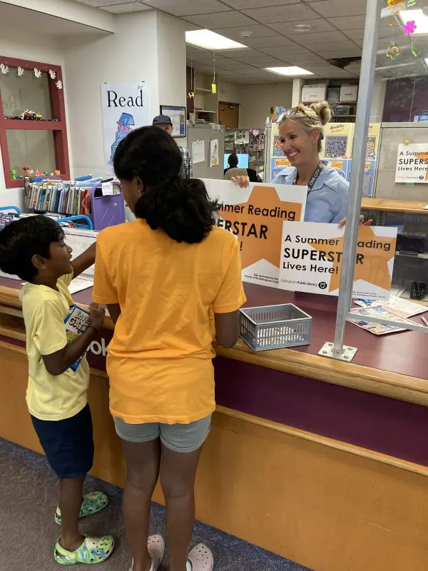Two kids receive reading awards from behind a library counter.
