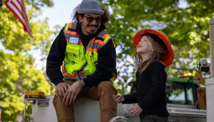 A construction worker and child smile on a truck