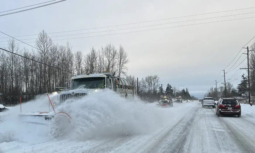 Three large snow plows in a line driving down snowy street