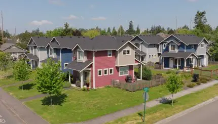 several two-story homes built fairly close together with lawns, trees and sidewalk near by