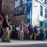 A crowd of people look at murals in an alley
