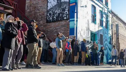 A crowd of people look at murals in an alley