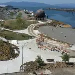 An aerial view of a waterfront park with a large, round, mental sculpture