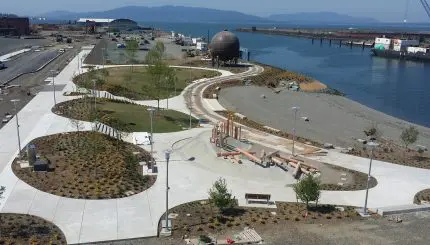 An aerial view of a waterfront park with a large, round, mental sculpture