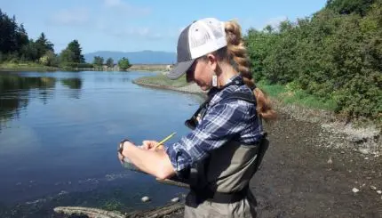 Woman writing on clipboard next to a river