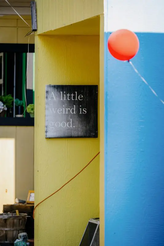 A sign on the side of a tiny house reading "a little weird is cool"