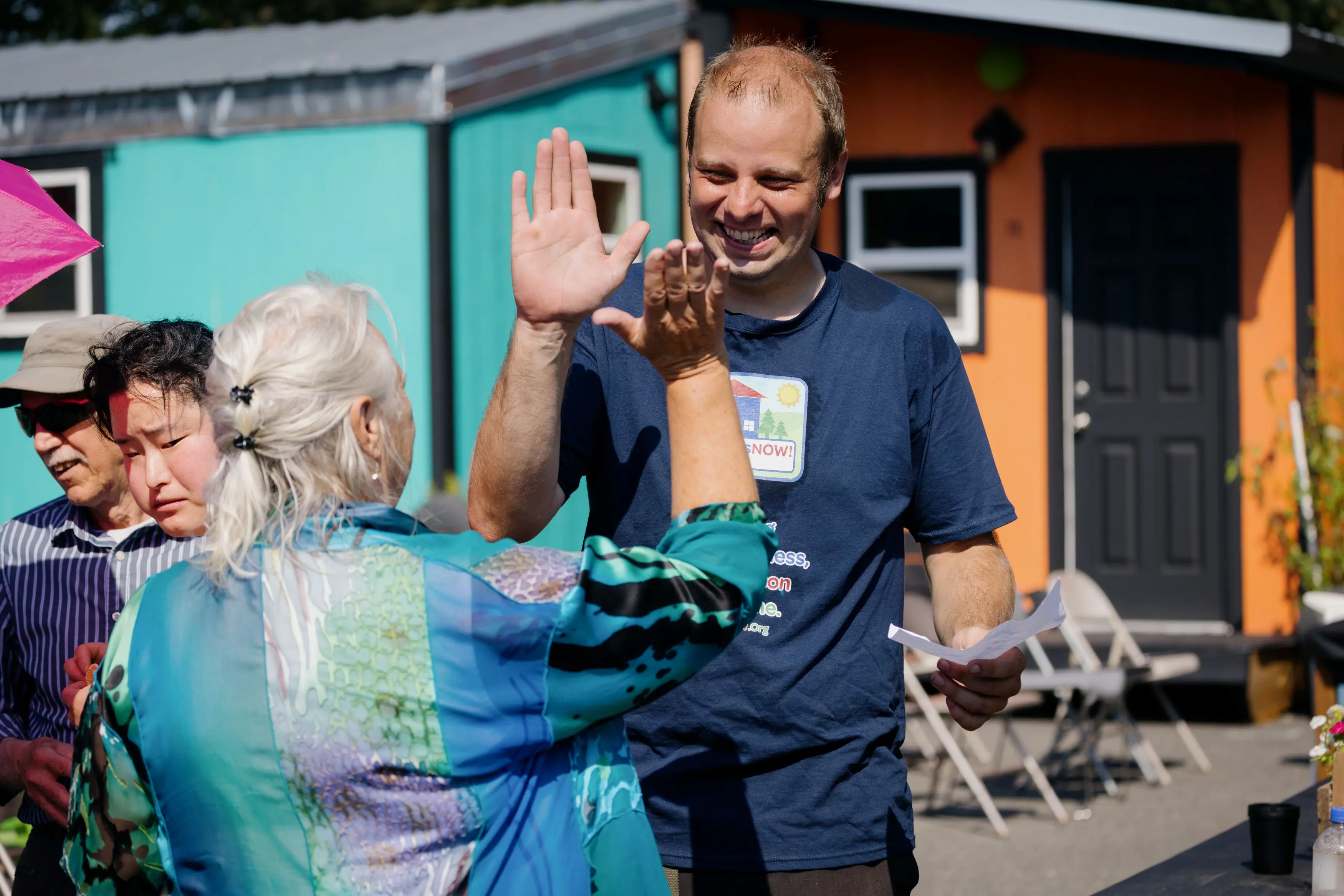 Two people high-five in front of several colorful tiny houses