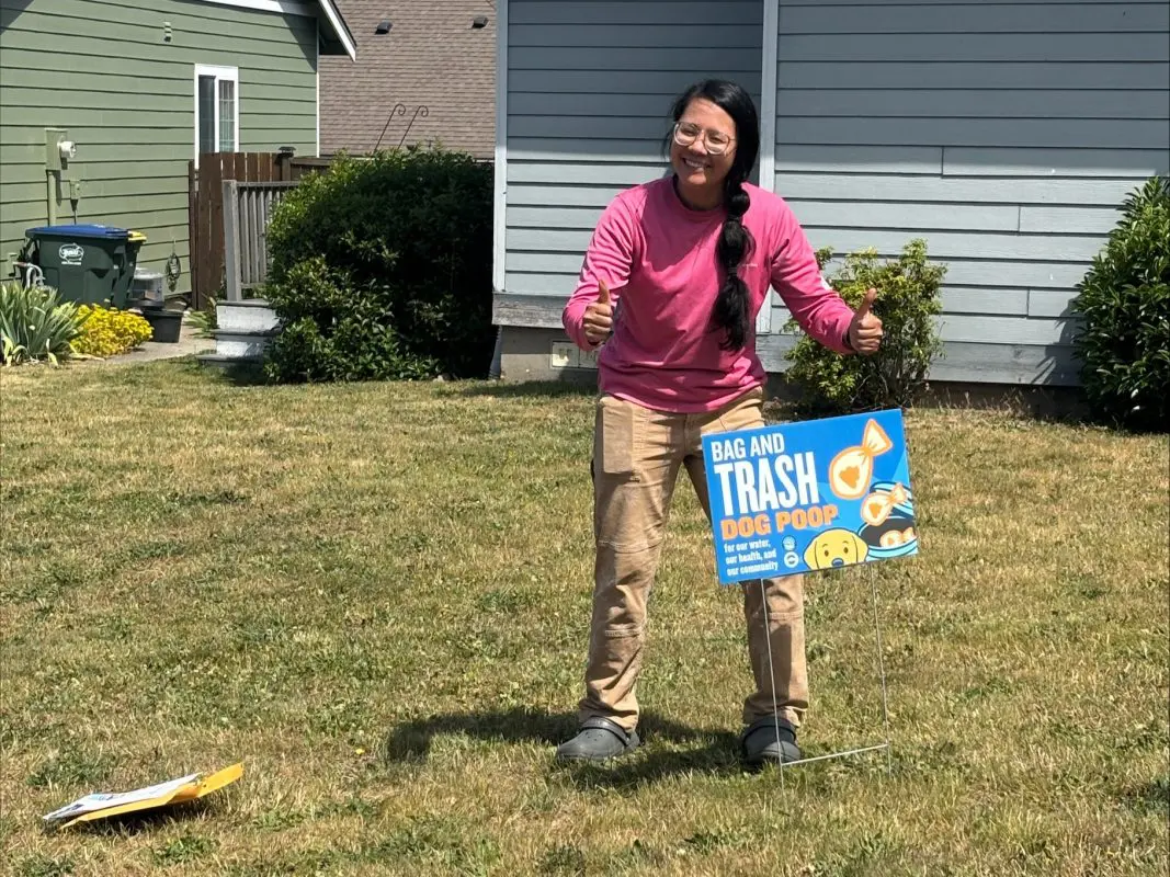 Person standing in yard next to a sign that says "scoop it bag it trash it"