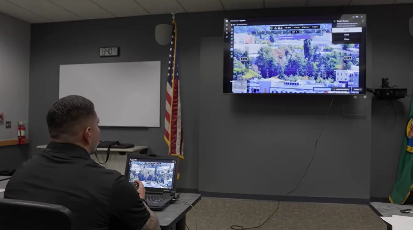 A police officer holds a controller and watches a tv screen showing a map