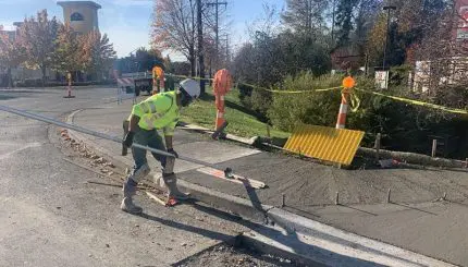 Worker using tool to flatten wet cement for new sidewalk