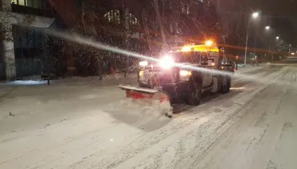 snow plow with head lights driving on snowy street in the dark